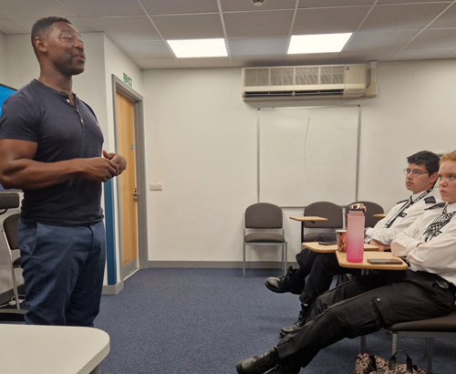 man speaking to an audience in a classroom setting with three attentive listeners engaged in a discussion