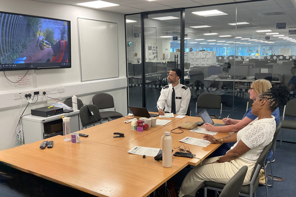 Meeting in a conference room with three people discussing and viewing a video on a large screen featuring various aspects of teamwork and collaboration
