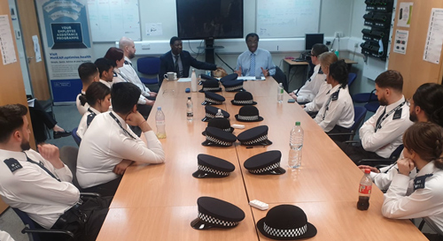 meeting room with police trainees seated at a long table wearing uniforms while engaging in discussion about law enforcement and community engagement