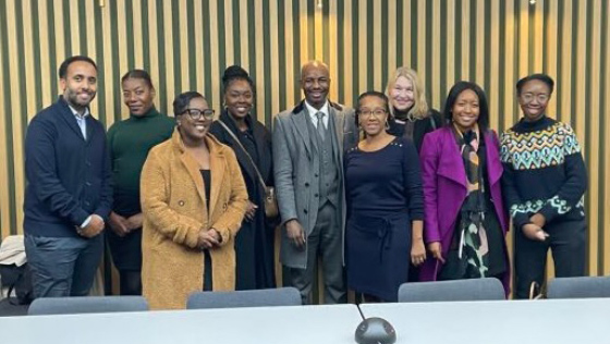 group photo of eight professionals standing together in an office setting with a conference table visible showcasing teamwork collaboration and diverse leadership