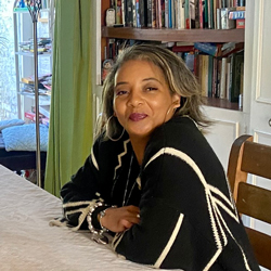woman sitting at a table in a cozy room with bookshelves smiling confidently showcasing a relaxed atmosphere inspired by artistic expression celebrating life and creativity related to the number 9