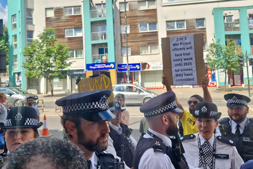police officers at a protest holding signs with funding demands and information about trials for misconduct in the community