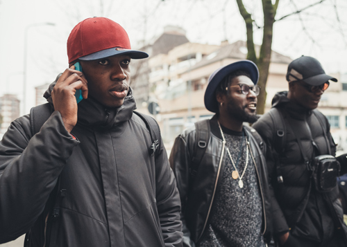 Three men walking on a city street wearing casual winter clothing with one man on the phone while the others smile and engage in conversation