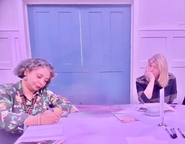 two people in a meeting writing notes at a table with a door in the background